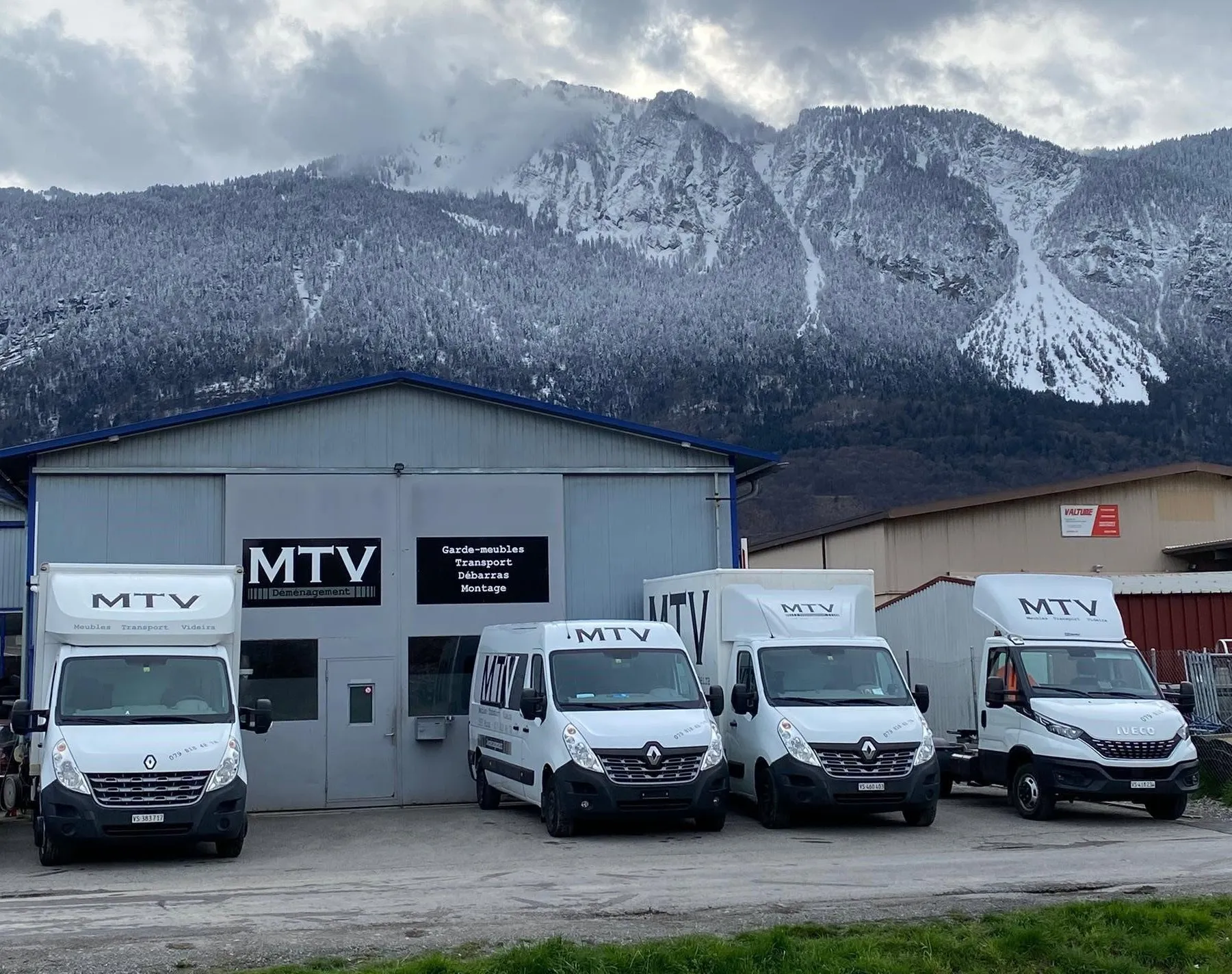 La flotte MTV alignée devant le dépôt en Valais, au pied de la montagne enneigée