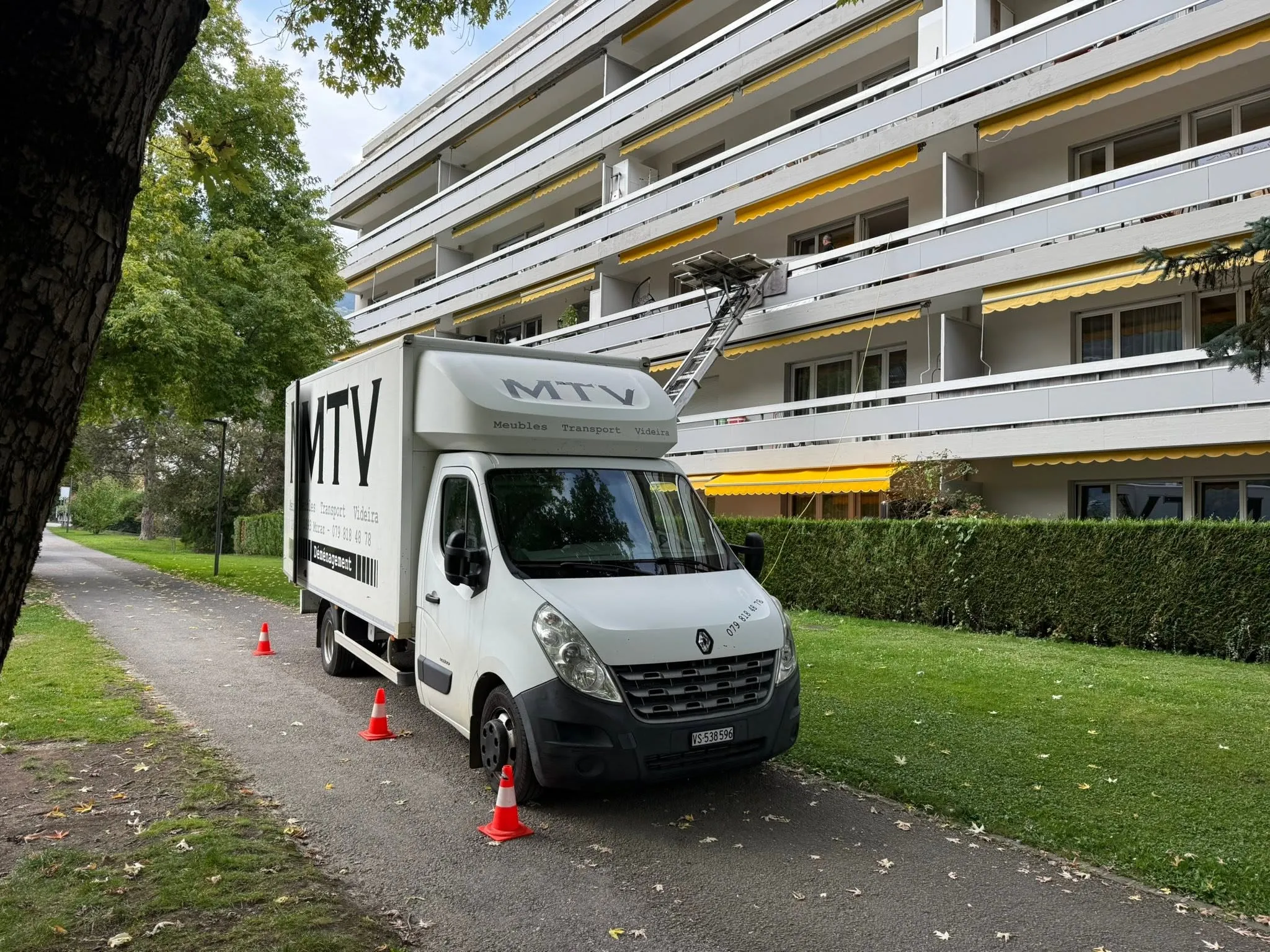 Camion de déménagement MTV avec monte-meuble déployé devant un immeuble en Valais